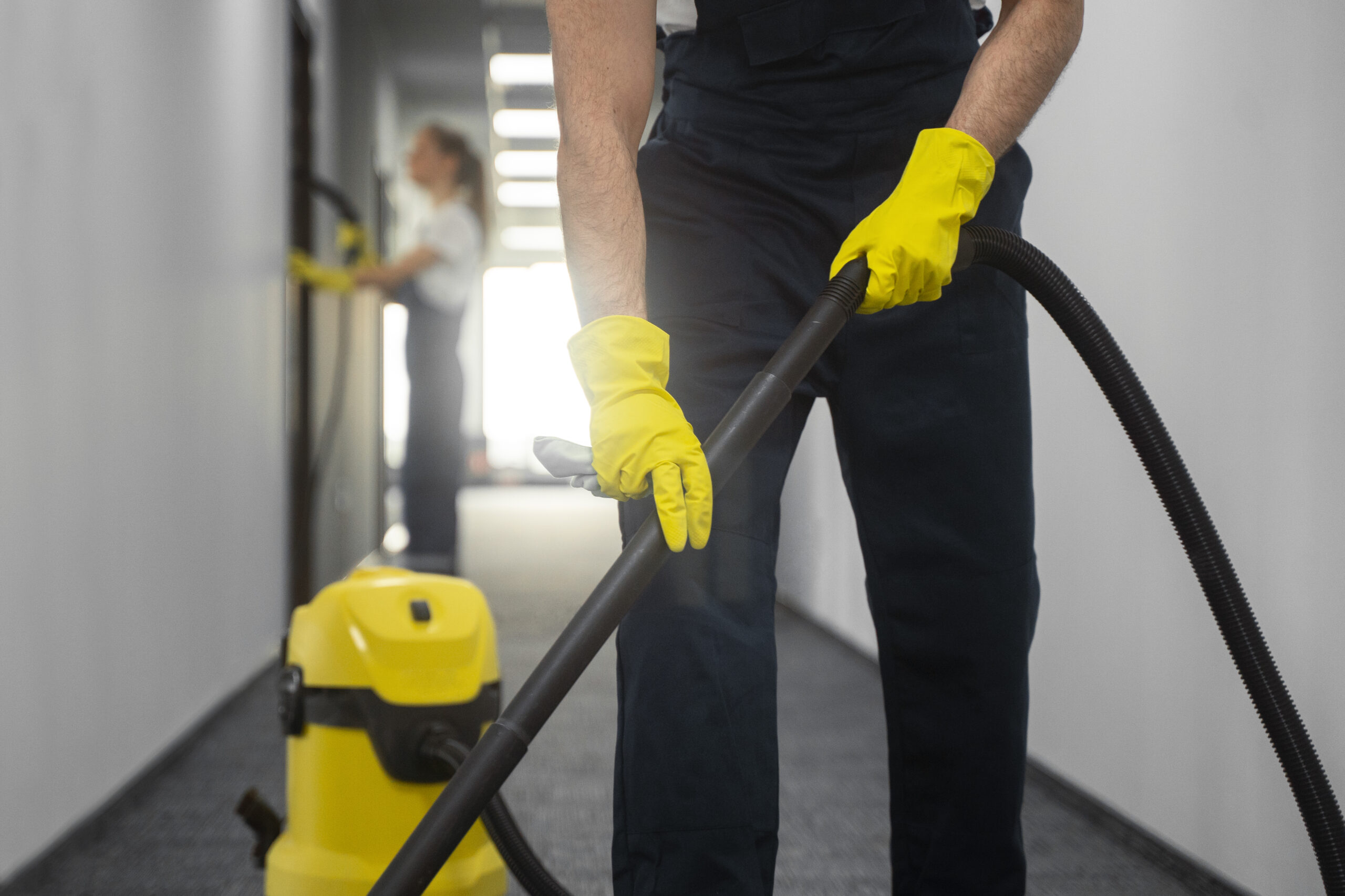 Professional cleaner with yellow vacuum using industrial equipment in bright white corridor hallway