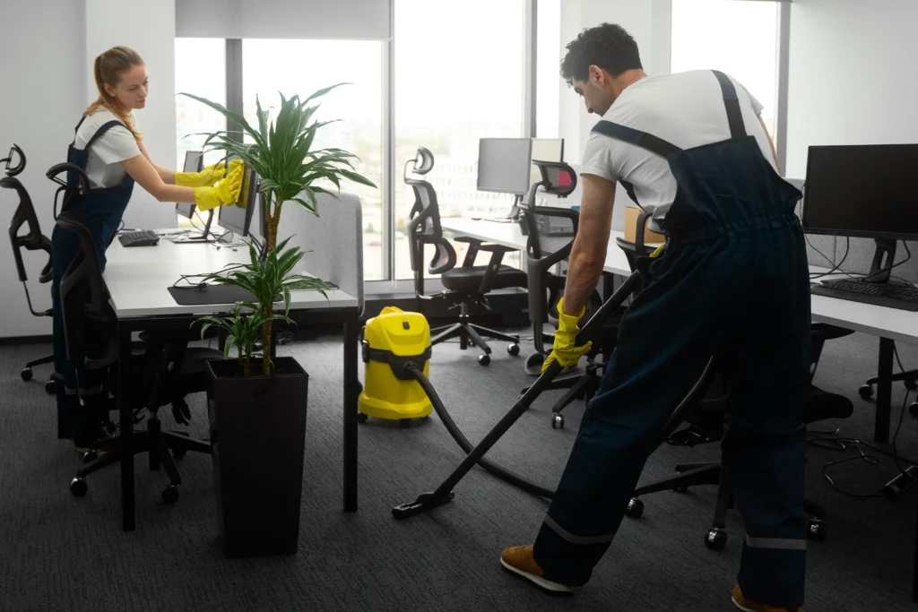 Professional office cleaners in uniforms vacuuming grey carpet with yellow vacuum cleaner - New Vision Cleaning