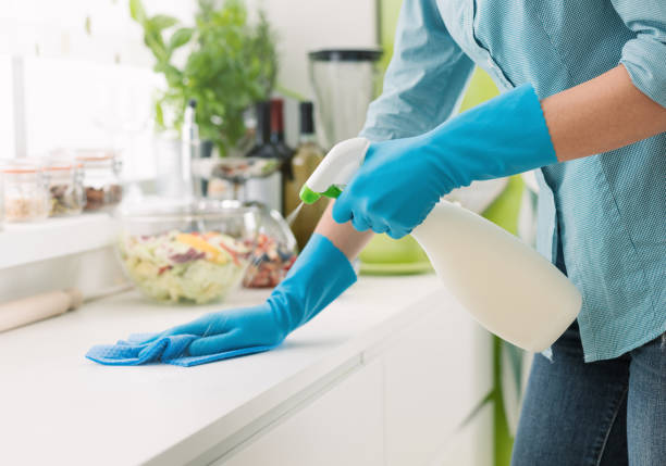 Professional cleaner in blue rubber gloves wiping white kitchen counters - cleaning service